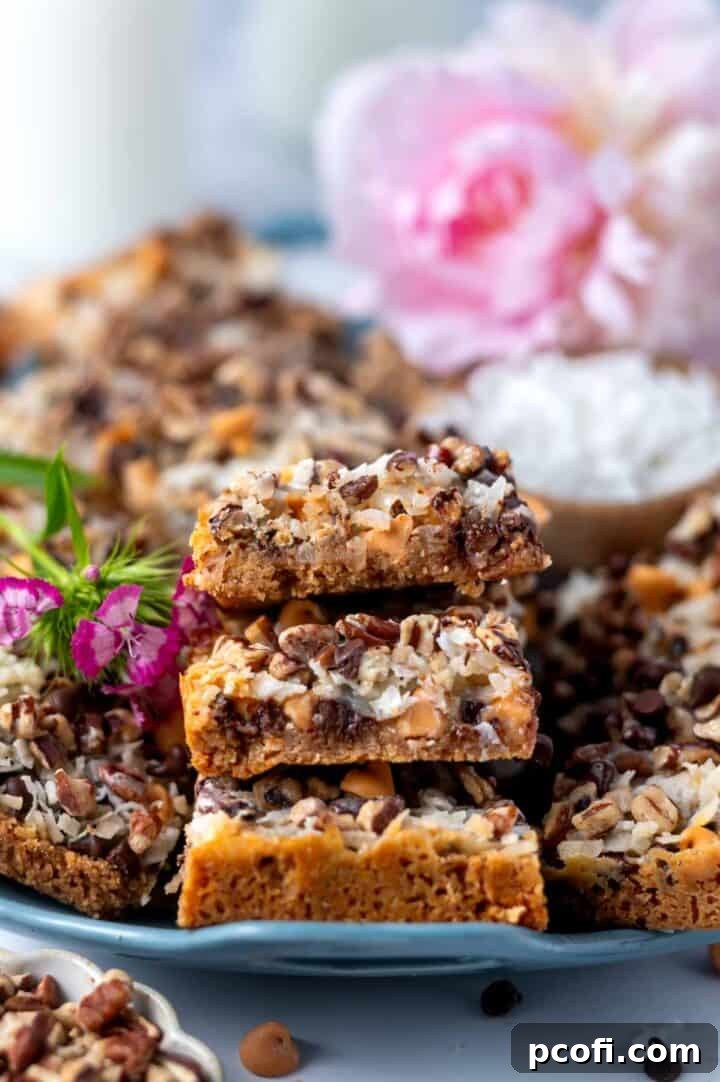 magic bars piled on a platter with a bowl of coconut, pecans and fresh pink flowers in the background