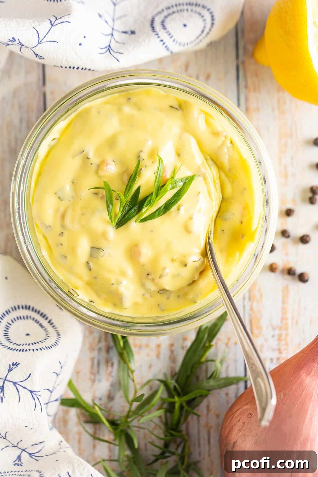 Homemade Béarnaise sauce in a glass bowl with a spoon inside.