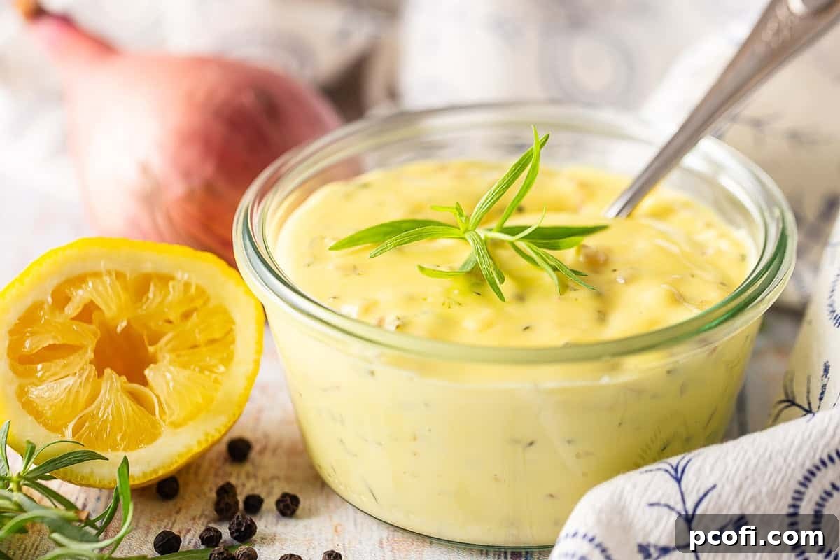 Bearnaise sauce in a small glass dish with a spoon inside, a squeezed lemon beside it, and some tarragon on top.