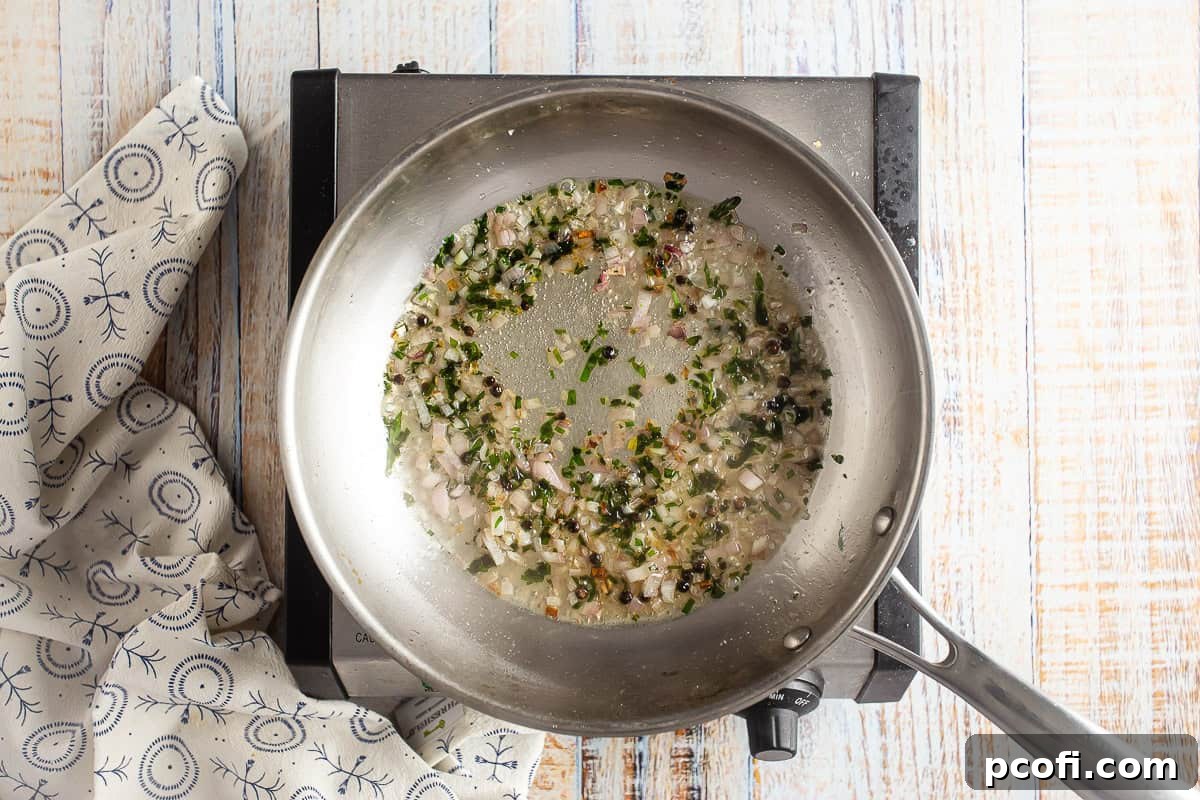 Butter, shallot, and tarragon being sautéed in a large stainless skillet.