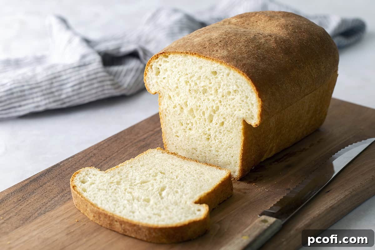 A freshly baked loaf of Homemade Potato Bread on a wooden cutting board, showcasing its golden crust and soft texture, with a few slices already cut.