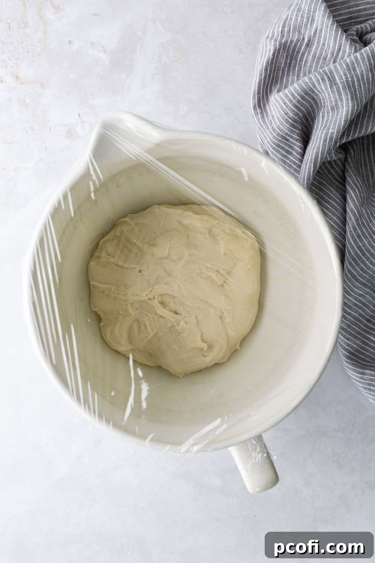 Potato bread dough shaped into a ball and placed in a lightly greased bowl, covered securely with plastic wrap for its first rise.