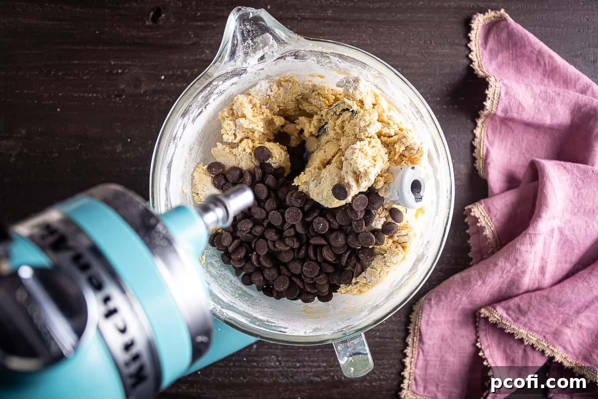Chocolate chips being mixed into the cookie dough in a stand mixer.