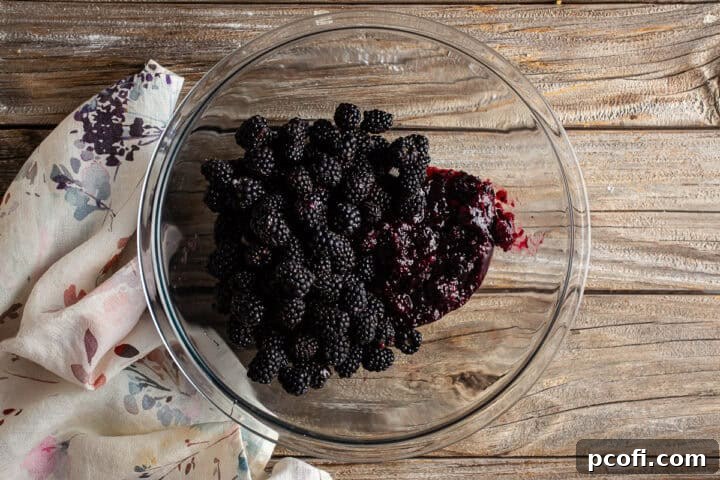 Fresh berries in a large glass bowl with the cooked blackberry pie filling.