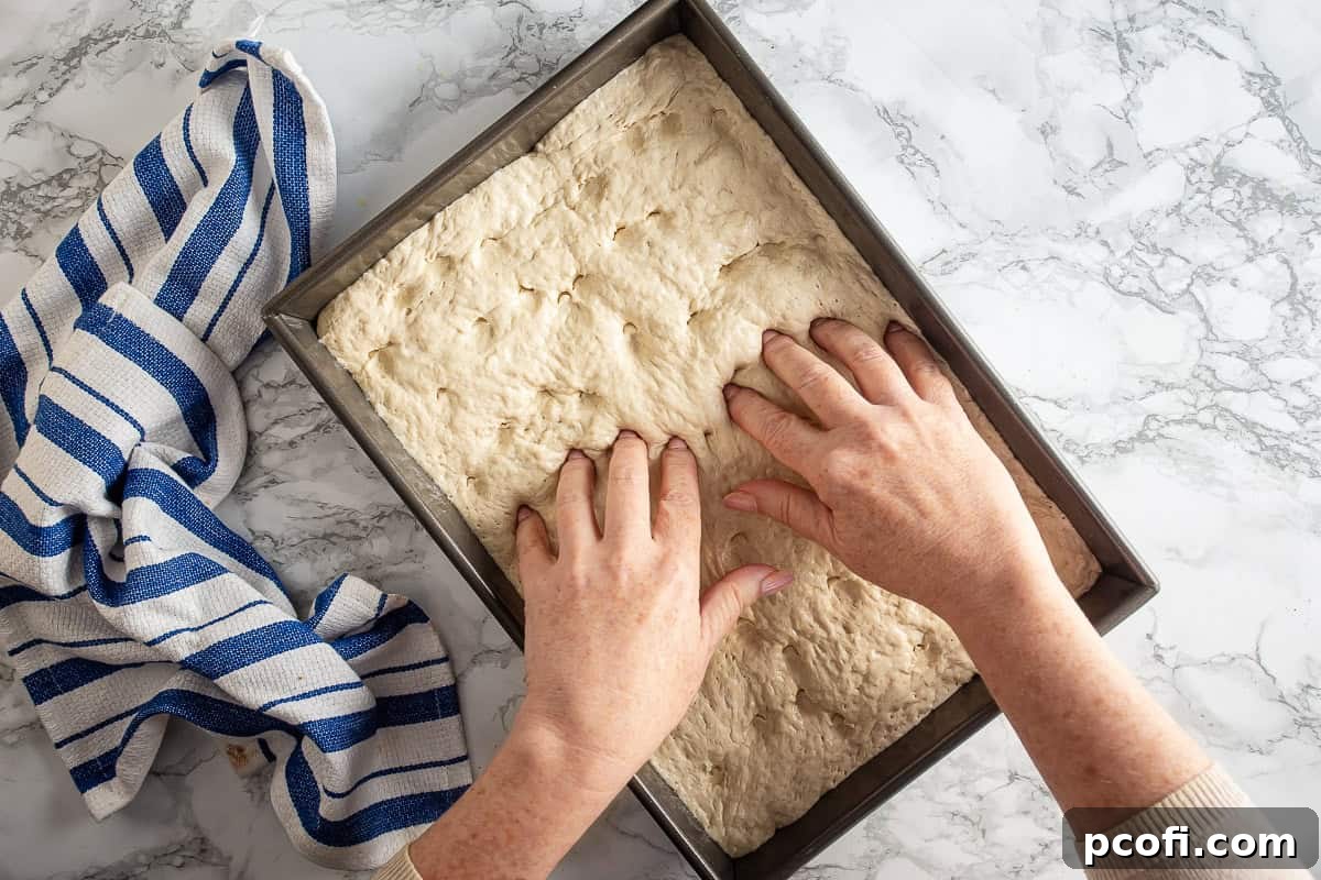 Creating dimples in the dough for Philadelphia Tomato Pie Pizza, showing the risen dough in a baking pan.