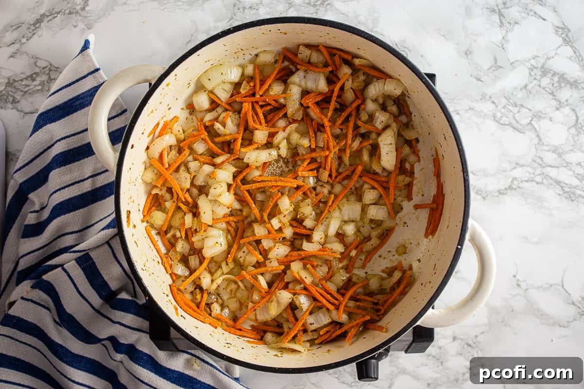 Vegetables being sauteed in a Dutch Oven for the sauce for Tomato Pie Pizza, showing onions and carrots cooking.