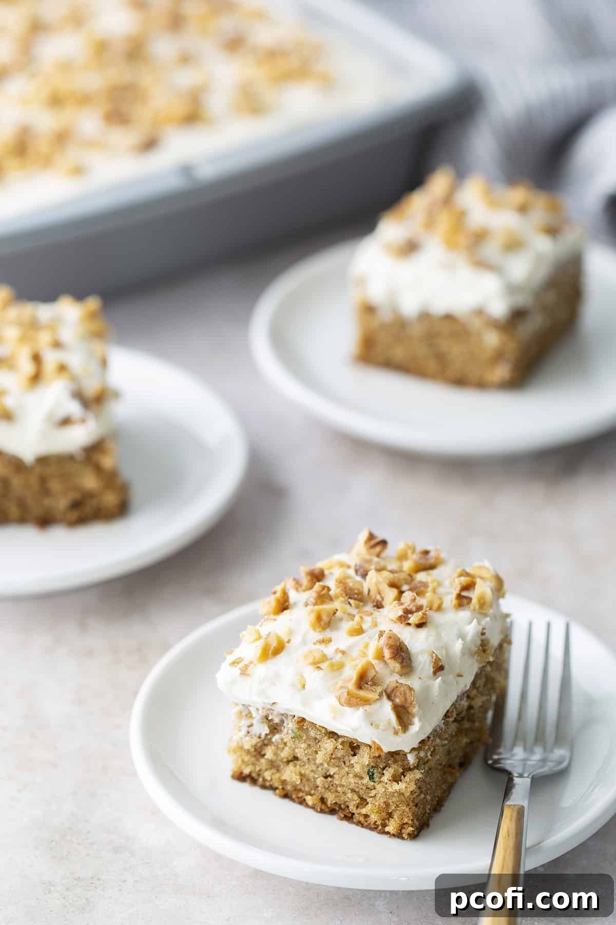 A beautifully frosted Zucchini Cake slice on a plate, ready to be enjoyed with a fork.