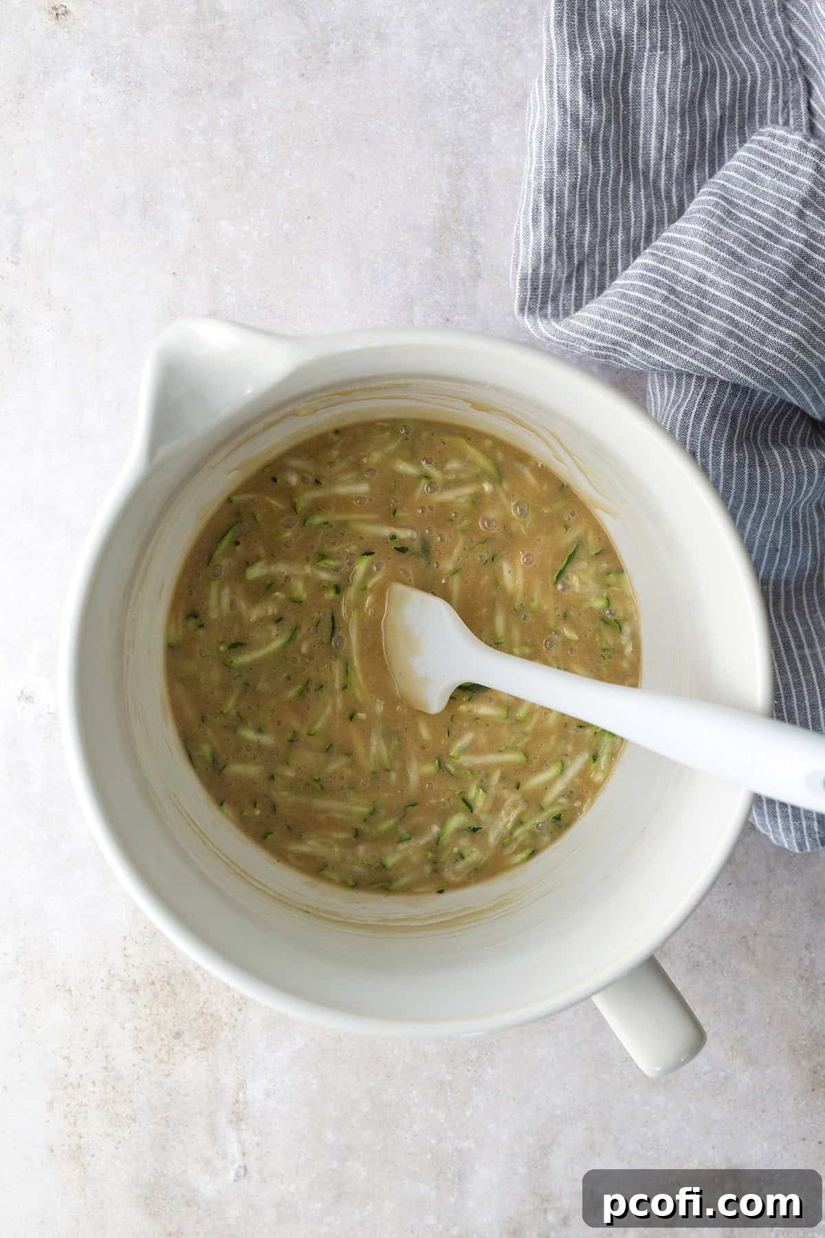 Wet ingredients for zucchini cake (eggs, oil, butter, sugars, vanilla) mixed in a bowl, with grated zucchini about to be added.