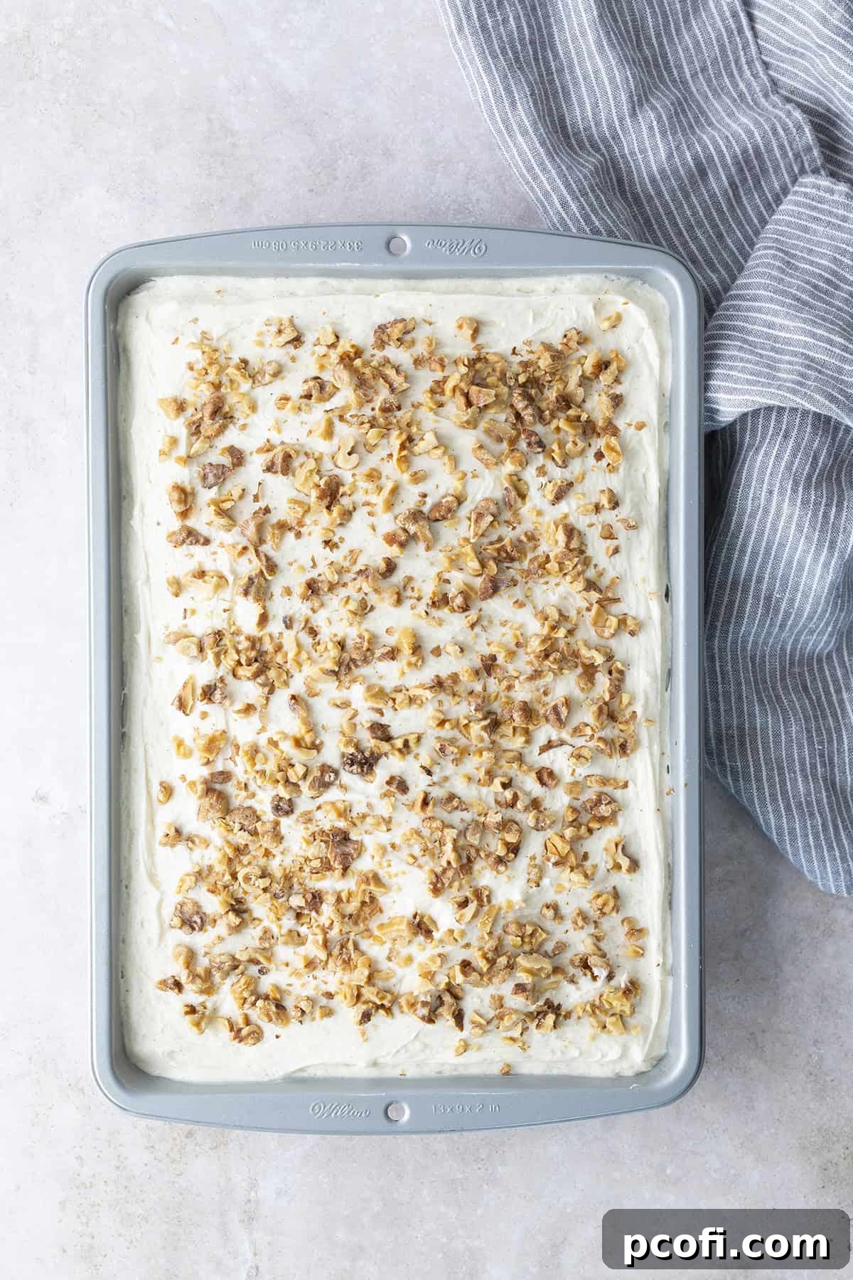 Chopped walnuts scattered over the top of a frosted zucchini cake, ready for serving.