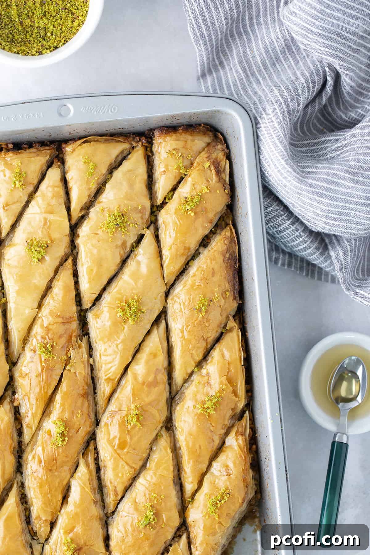 Freshly baked baklava in a baking pan, beautifully sliced into diamond shapes and glistening with honey syrup.