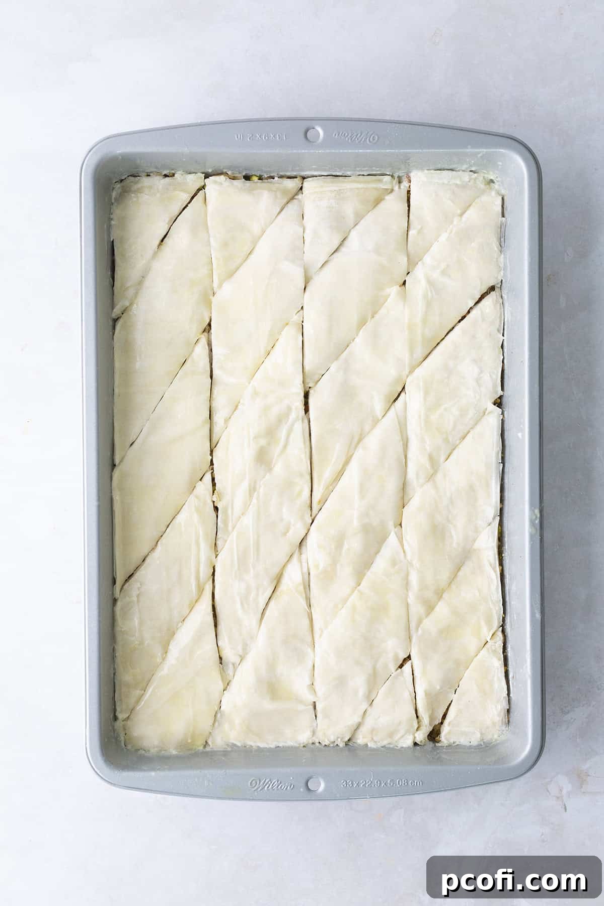 Unbaked baklava in the pan, meticulously pre-sliced into individual diamond shapes before baking, ready for the oven.