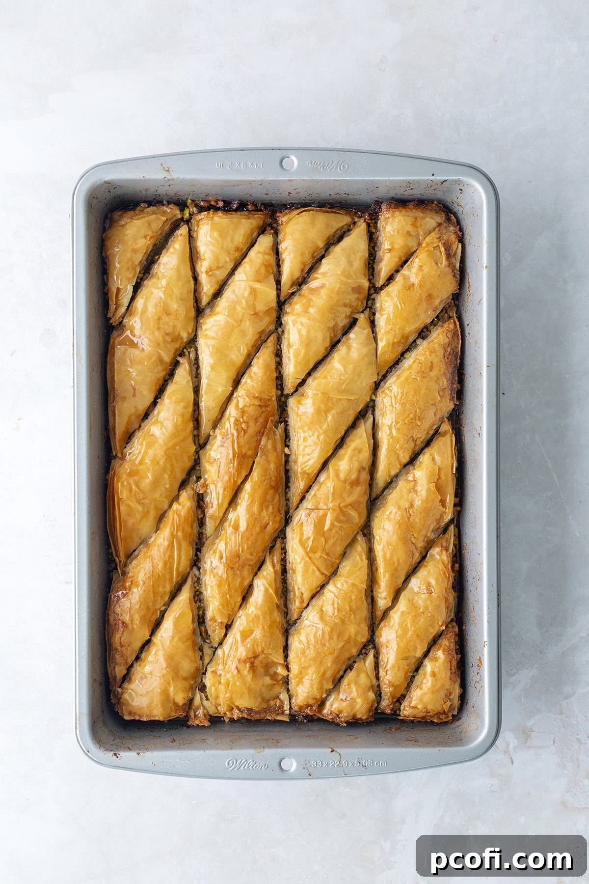 Cool honey-lemon syrup being generously poured over hot, freshly baked baklava in a pan, creating a satisfying sizzle.