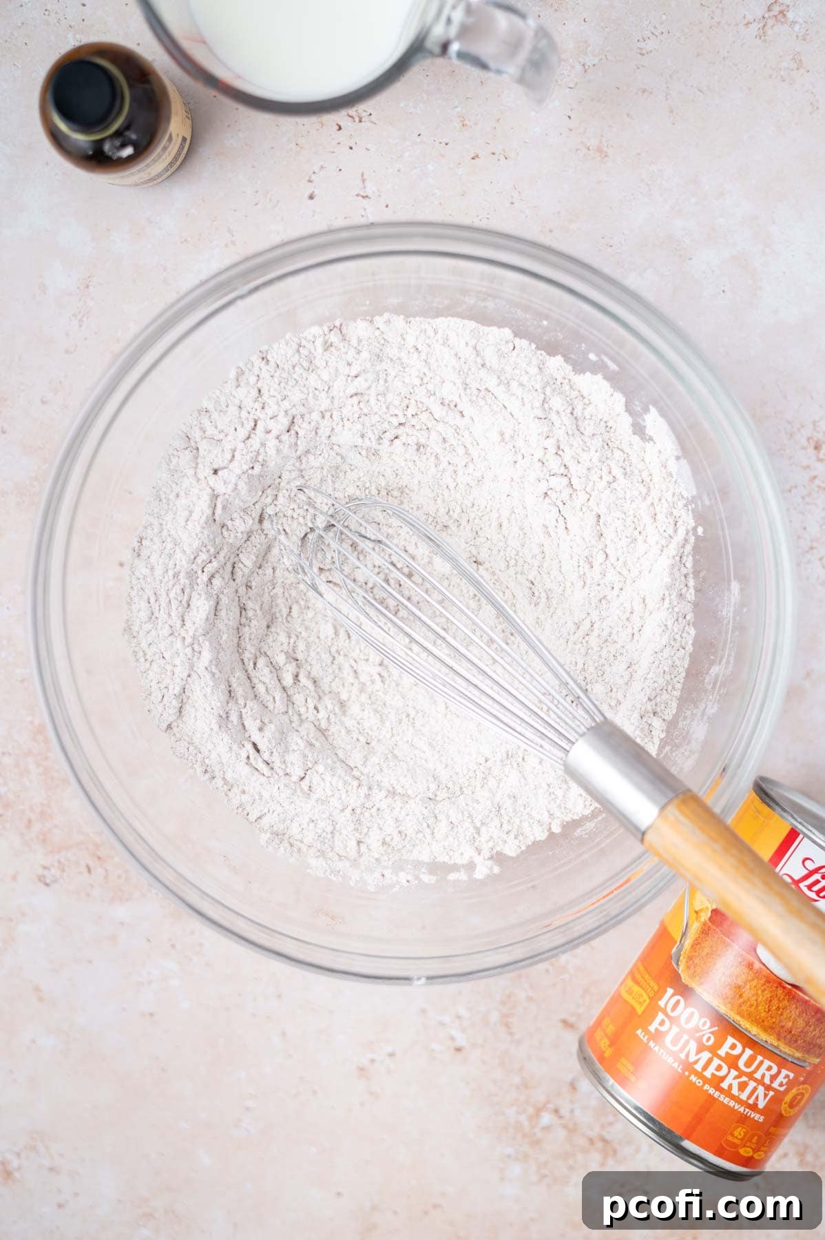 Dry ingredients including flour, spices, baking powder, and salt are whisked together in a large mixing bowl.