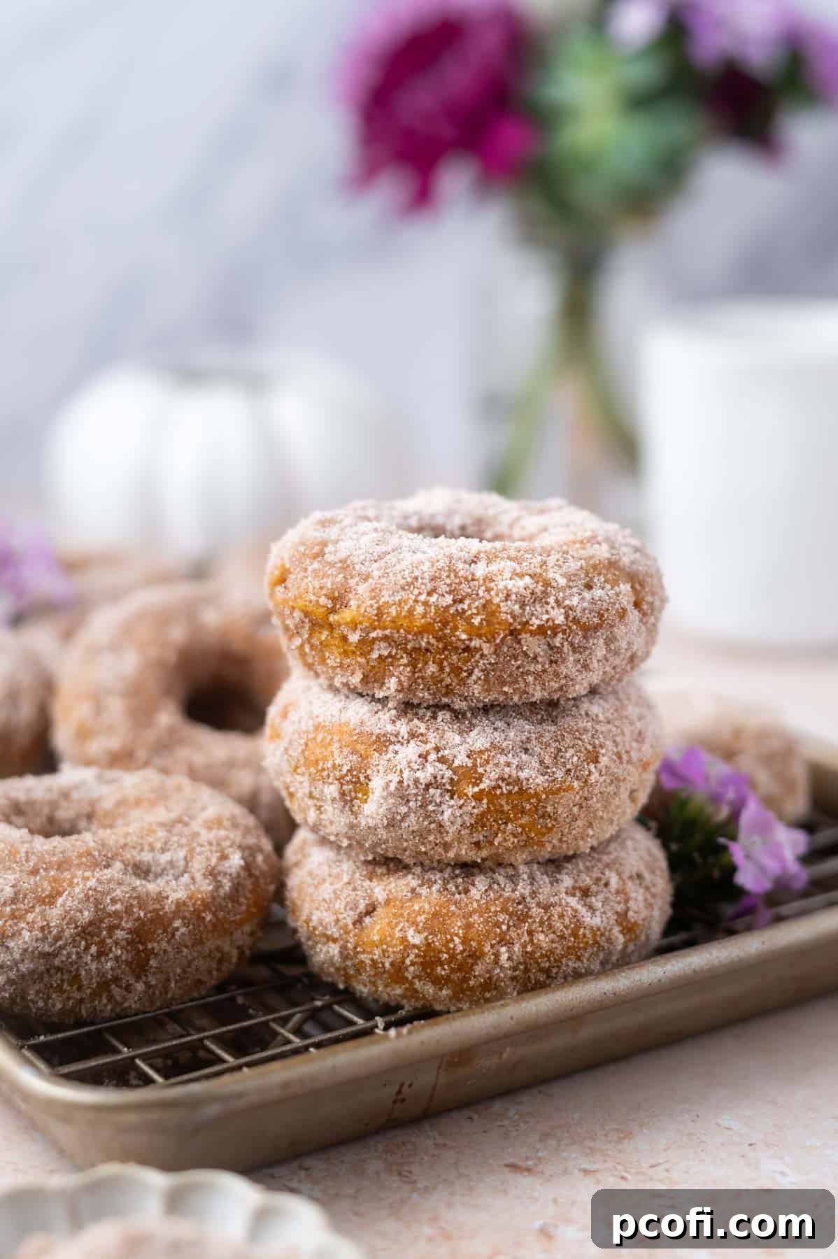A beautiful stack of golden-brown baked pumpkin donuts, glistening with spiced sugar, resting on a wire rack.