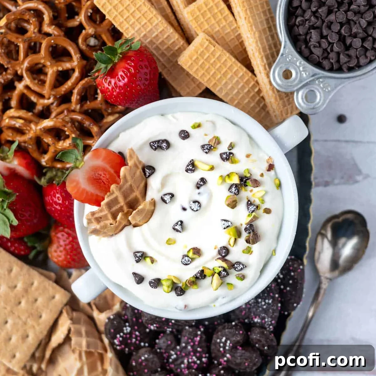 overhead look at cannoli dip with pistachios and chocolate chips on top. Surrounded by pretzels, strawberries and cookies.