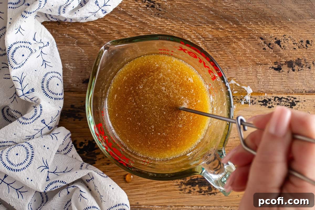 Wet ingredients for chocolate granola in a glass measuring cup with a hand whisking it together, showing a smooth mixture.