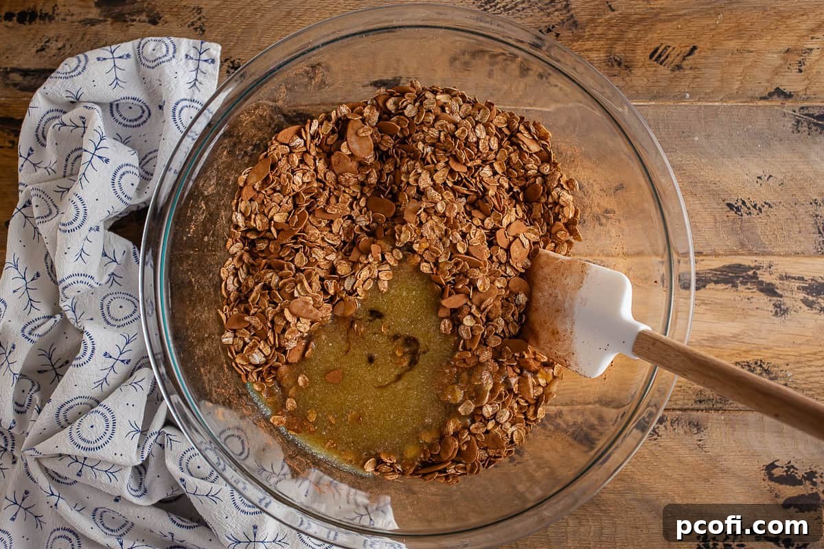Wet and dry ingredients for chocolate granola in a large glass bowl before being fully mixed, showing the liquid poured over the dry.