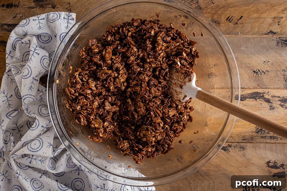 Ingredients for chocolate granola in a large glass bowl after being mixed together, showing a cohesive mixture.
