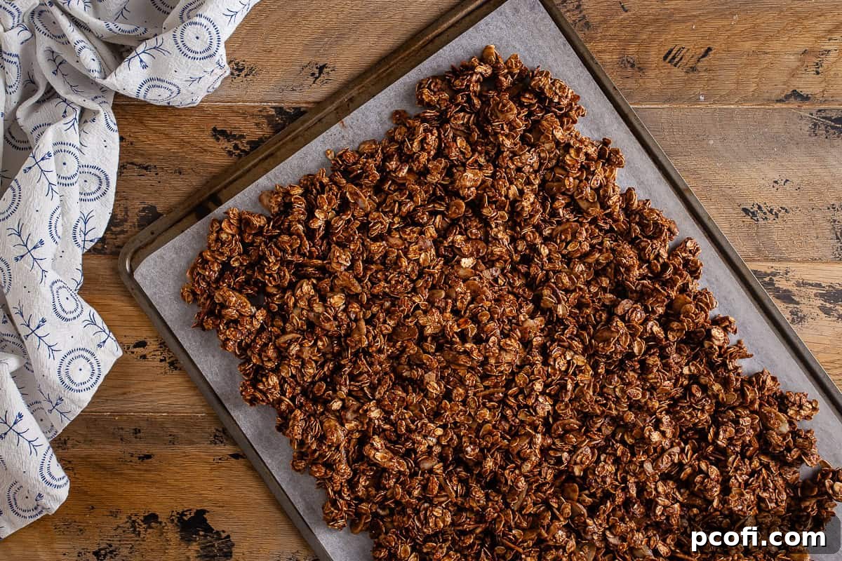 Chocolate granola on a parchment-lined baking sheet after being spread out into an even layer.
