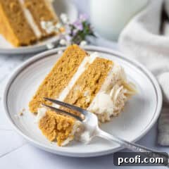 A slice of moist pumpkin layer cake on a plate with a fork, ready to be enjoyed.