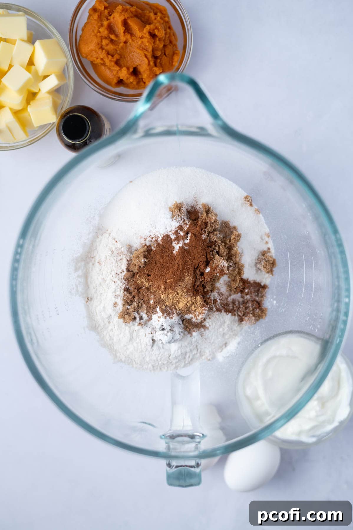 A large mixing bowl containing all the measured dry ingredients for the pumpkin layer cake, including flour, sugars, and spices, ready to be whisked.