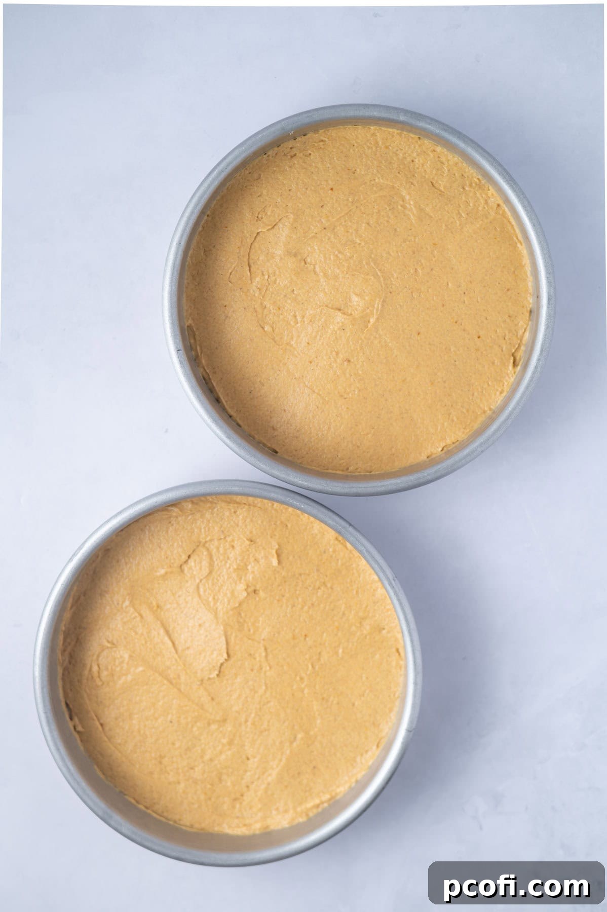 Two 8-inch round baking pans, perfectly filled with smooth pumpkin cake batter and ready to be placed in the oven.
