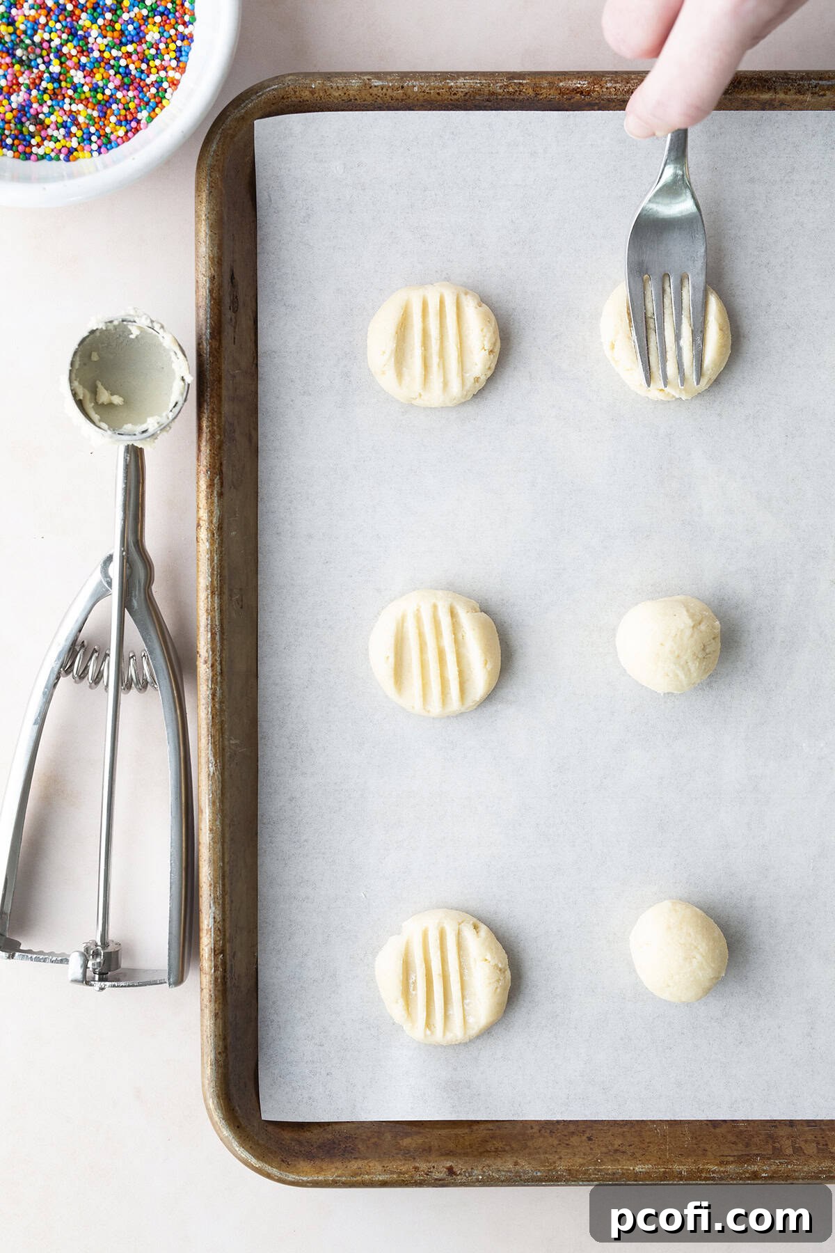 Portioned cookie dough on baking sheet with fork