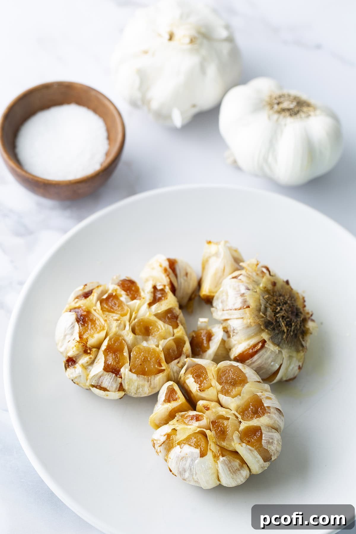 Several heads of beautifully roasted garlic on a plate, with some cloves already squeezed out.