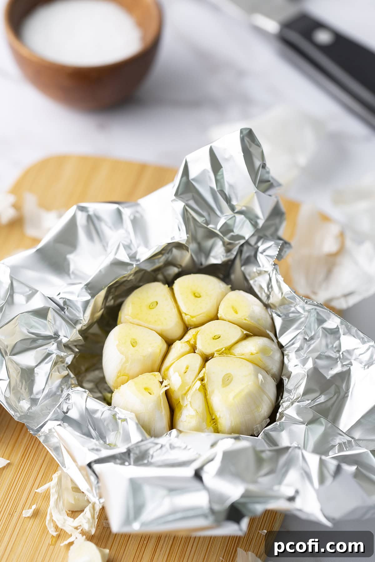 Olive oil being drizzled generously on top of the sliced garlic head in foil.