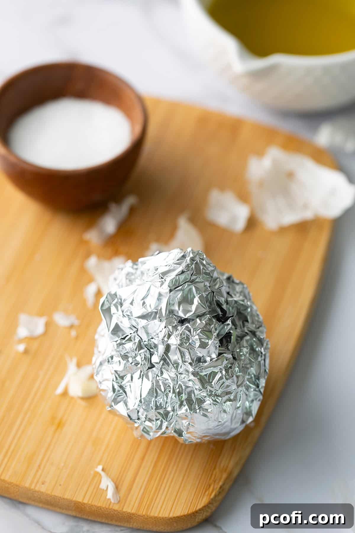 Garlic head fully wrapped in aluminum foil, ready for roasting.
