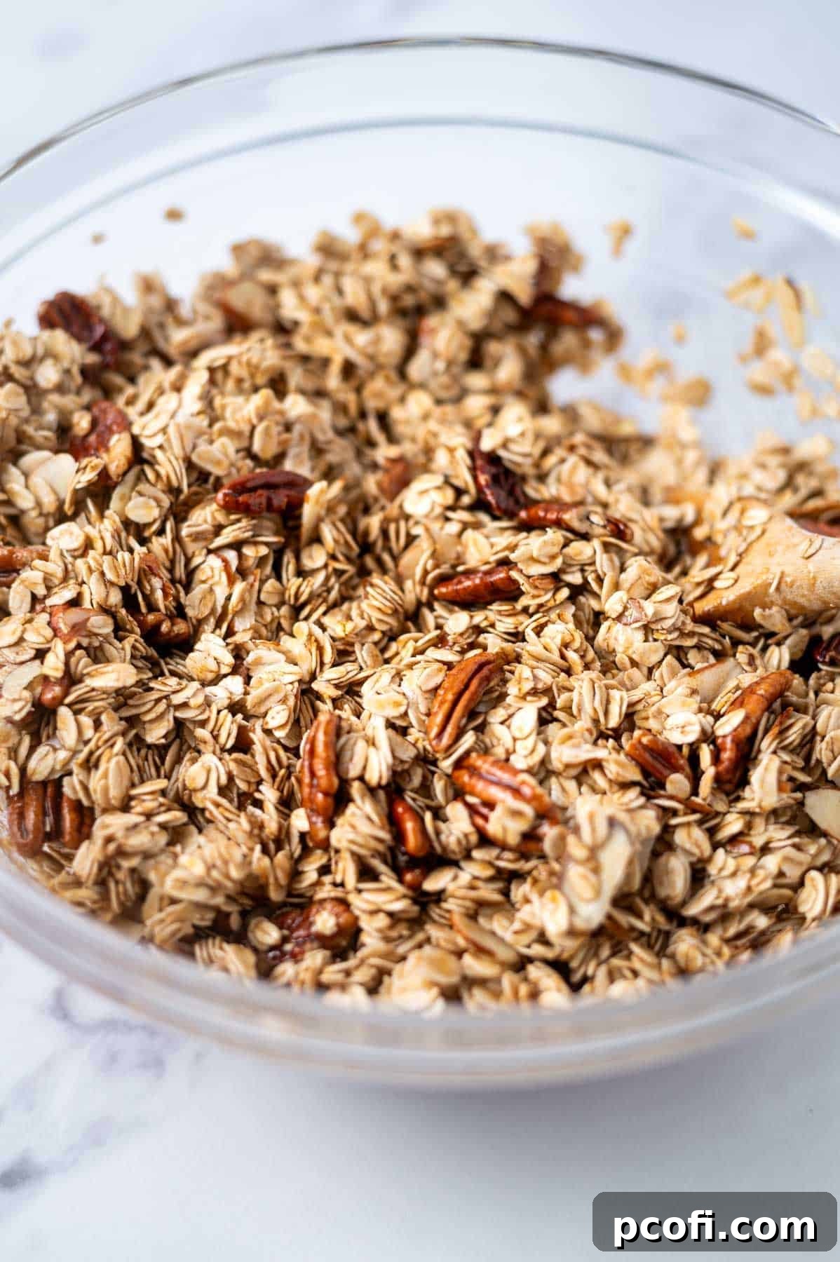 Wet and dry ingredients for maple granola are mixed together in a bowl, coating the oats and nuts.