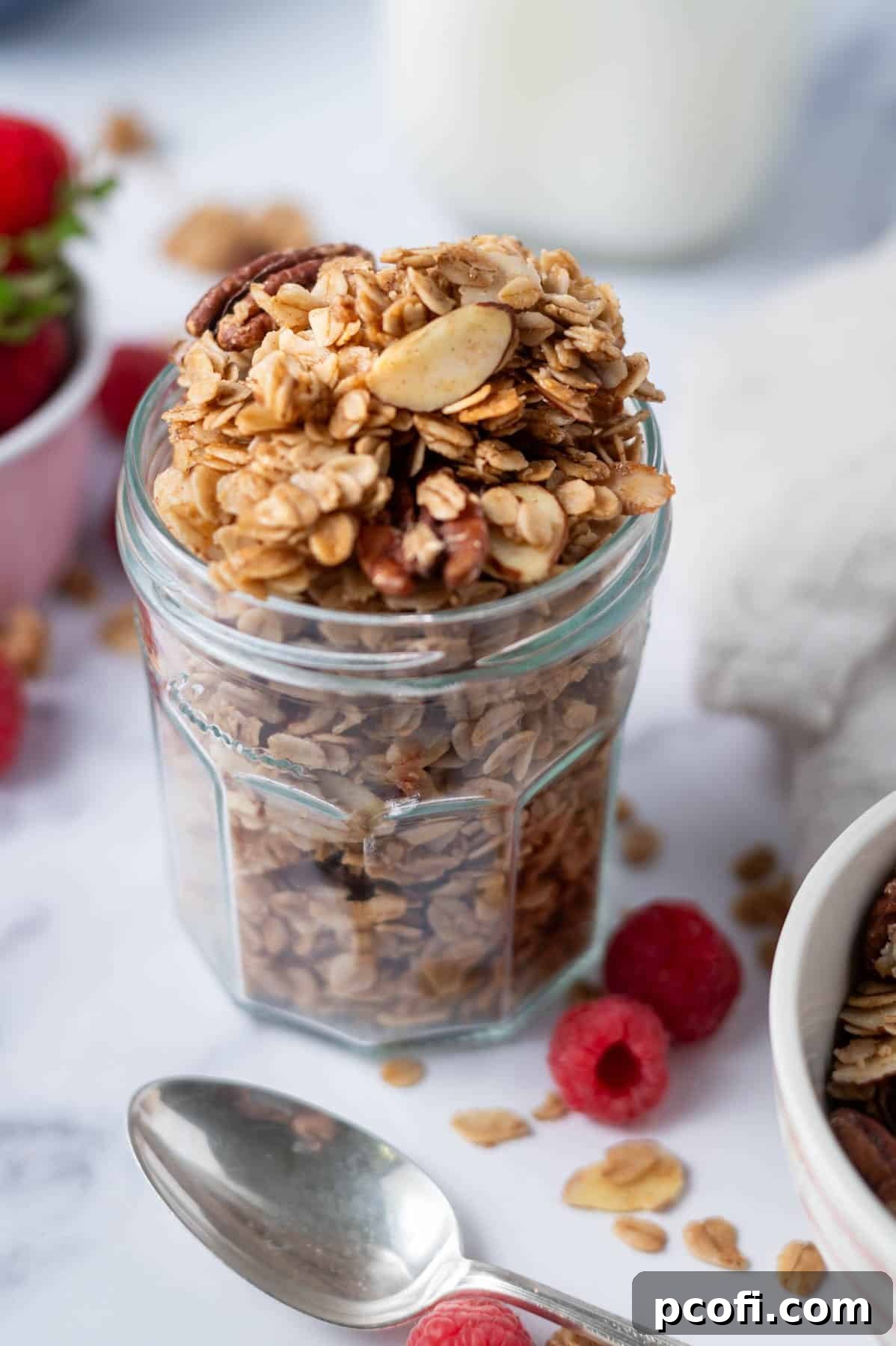 A glass jar filled with homemade maple granola and a wooden spoon, showcasing its perfect clusters.