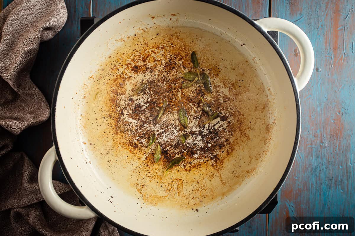 Fresh sage leaves frying in hot bacon fat within a large Dutch oven, preparing for pumpkin risotto.