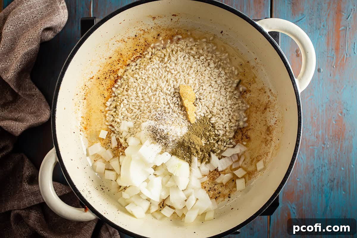Arborio rice, chopped onions, and a medley of seasonings being combined in a large Dutch oven, ready for sautéing for pumpkin risotto.
