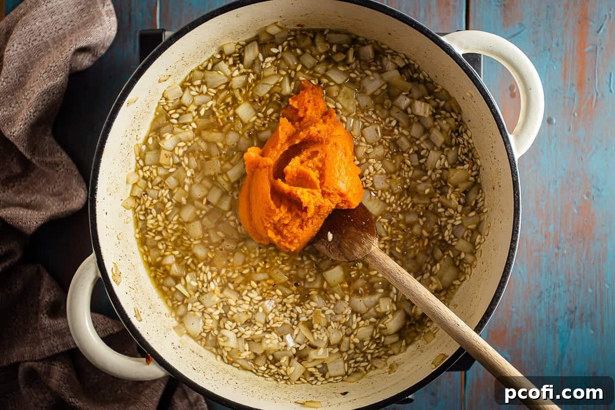 Creamy pumpkin puree being stirred into the sautéed rice and onions in a Dutch oven, initiating the pumpkin risotto phase.
