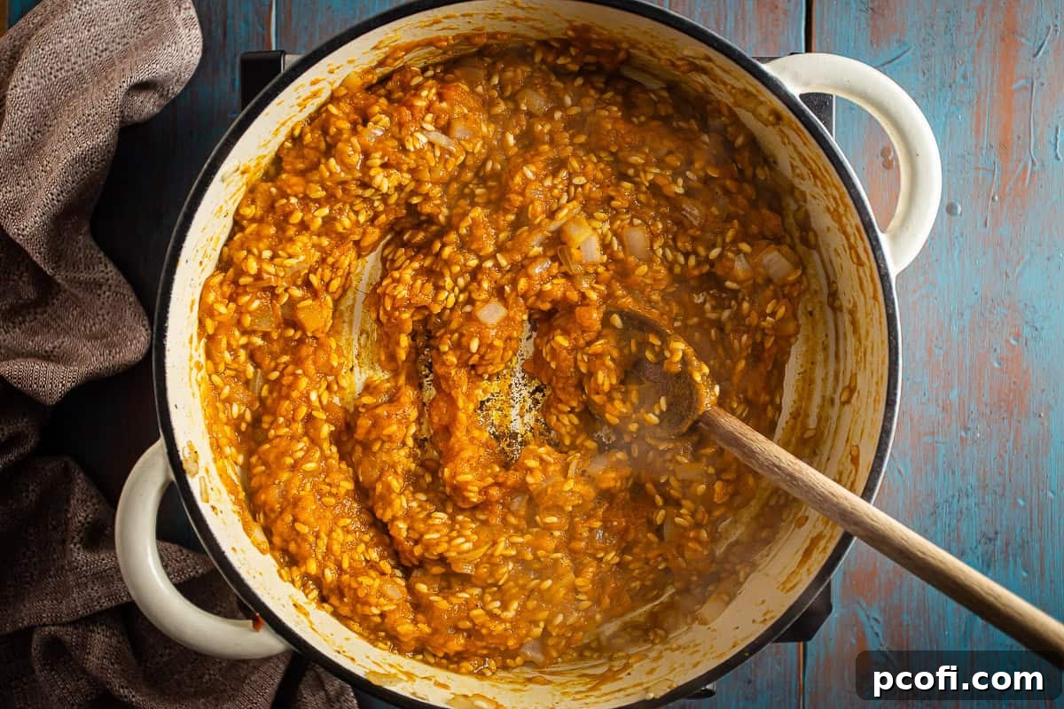Pumpkin risotto simmering gently in a Dutch oven after pumpkin and wine have been incorporated, showing its creamy transformation.
