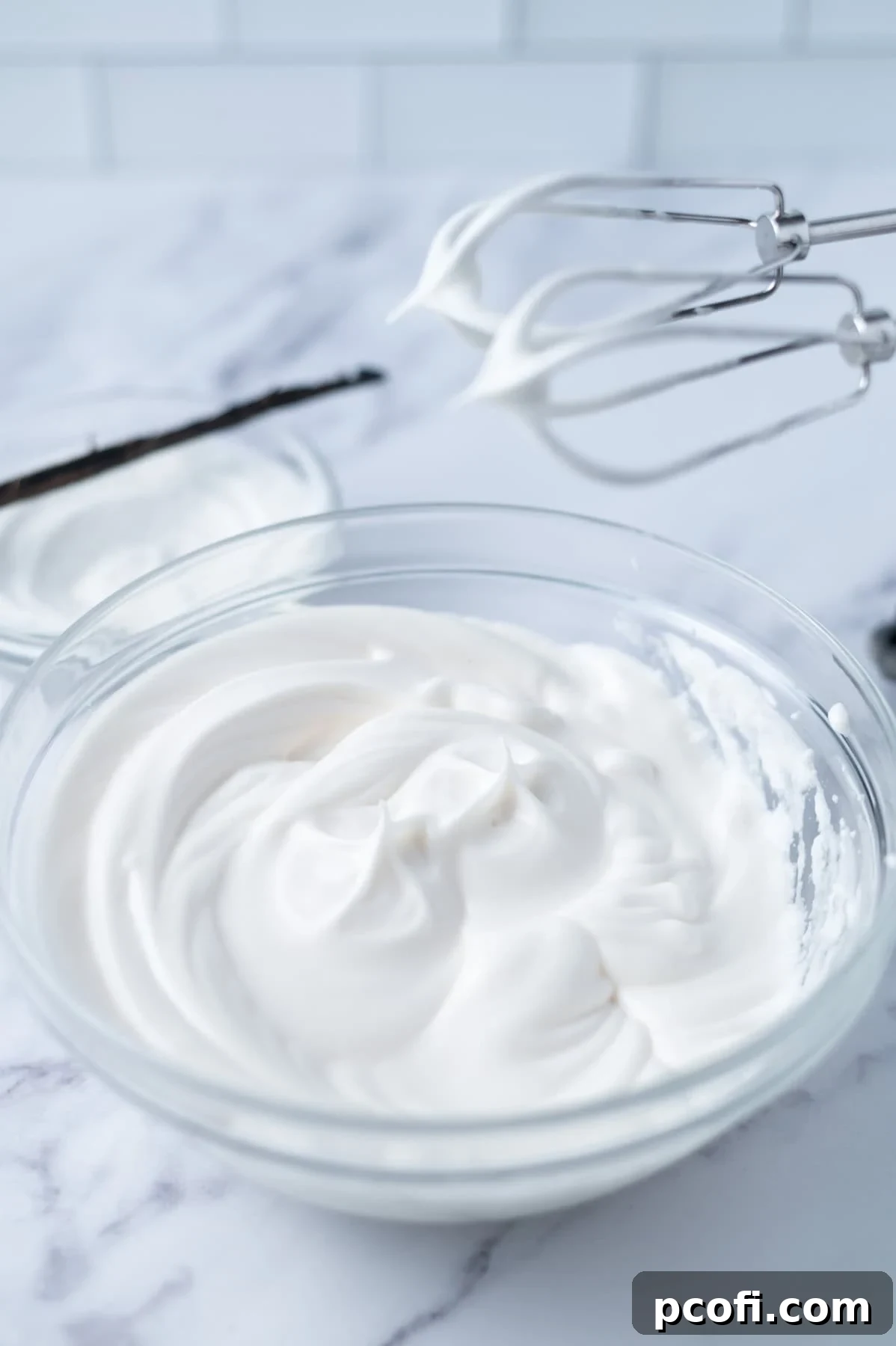 Whisked egg whites in a clear glass bowl, with a hand mixer resting nearby