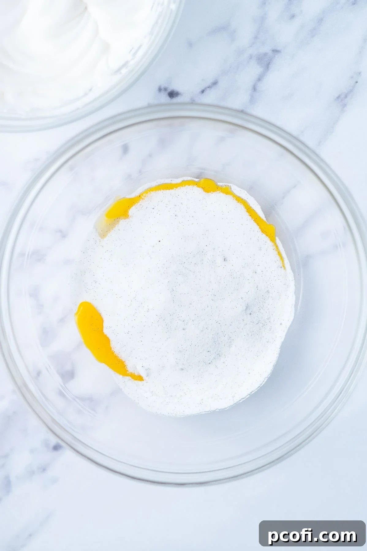 Egg yolks and vanilla-infused sugar being mixed in a glass bowl