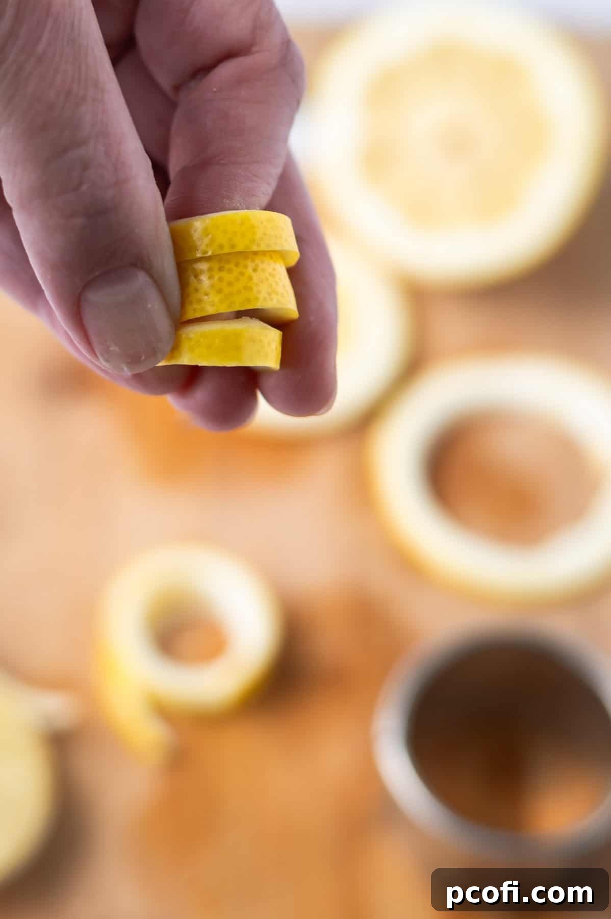 A hand demonstrating how to twist a lemon rind around an index finger to create a cocktail garnish.