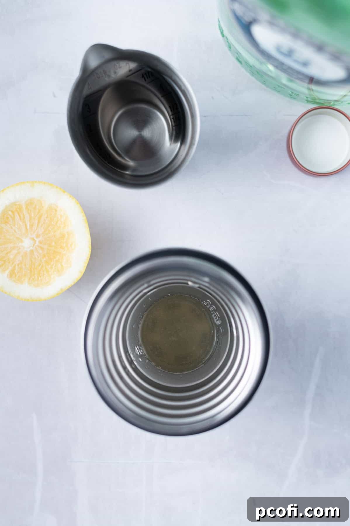 Overhead view of gin, simple syrup, and fresh lemon juice being poured into an ice-filled cocktail shaker.