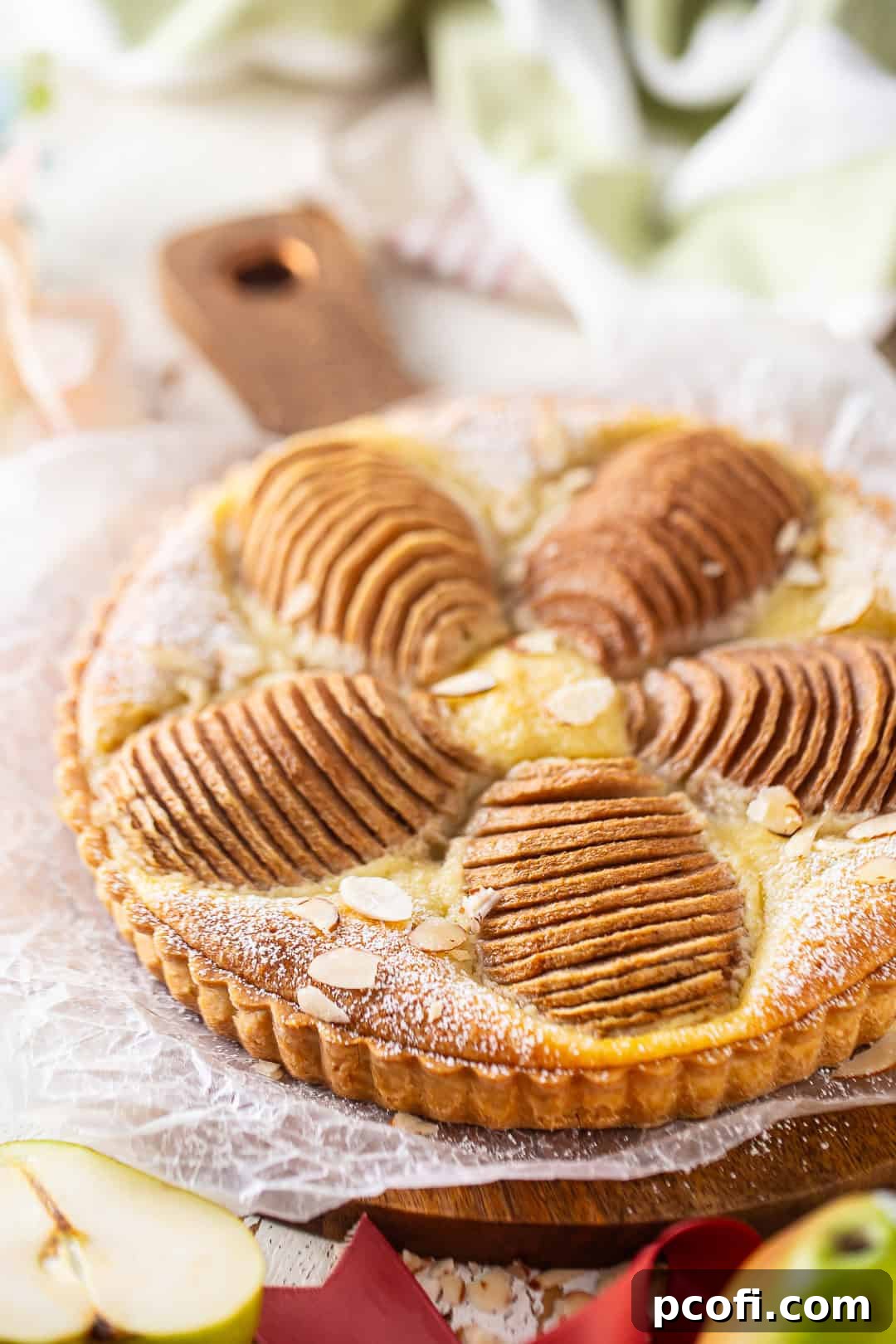 A beautifully baked pear tart, dusted with powdered sugar and garnished with sliced almonds, resting on an elegant serving tray.