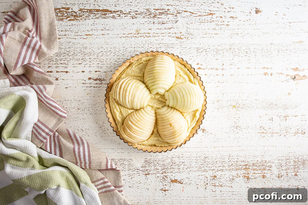 Thinly sliced pears meticulously fanned out over the almond frangipane filling in the tart shell, prior to baking.