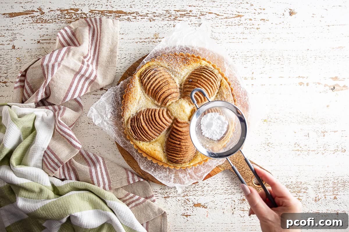 A freshly baked pear tart being dusted with powdered sugar for a beautiful and delicate finish.