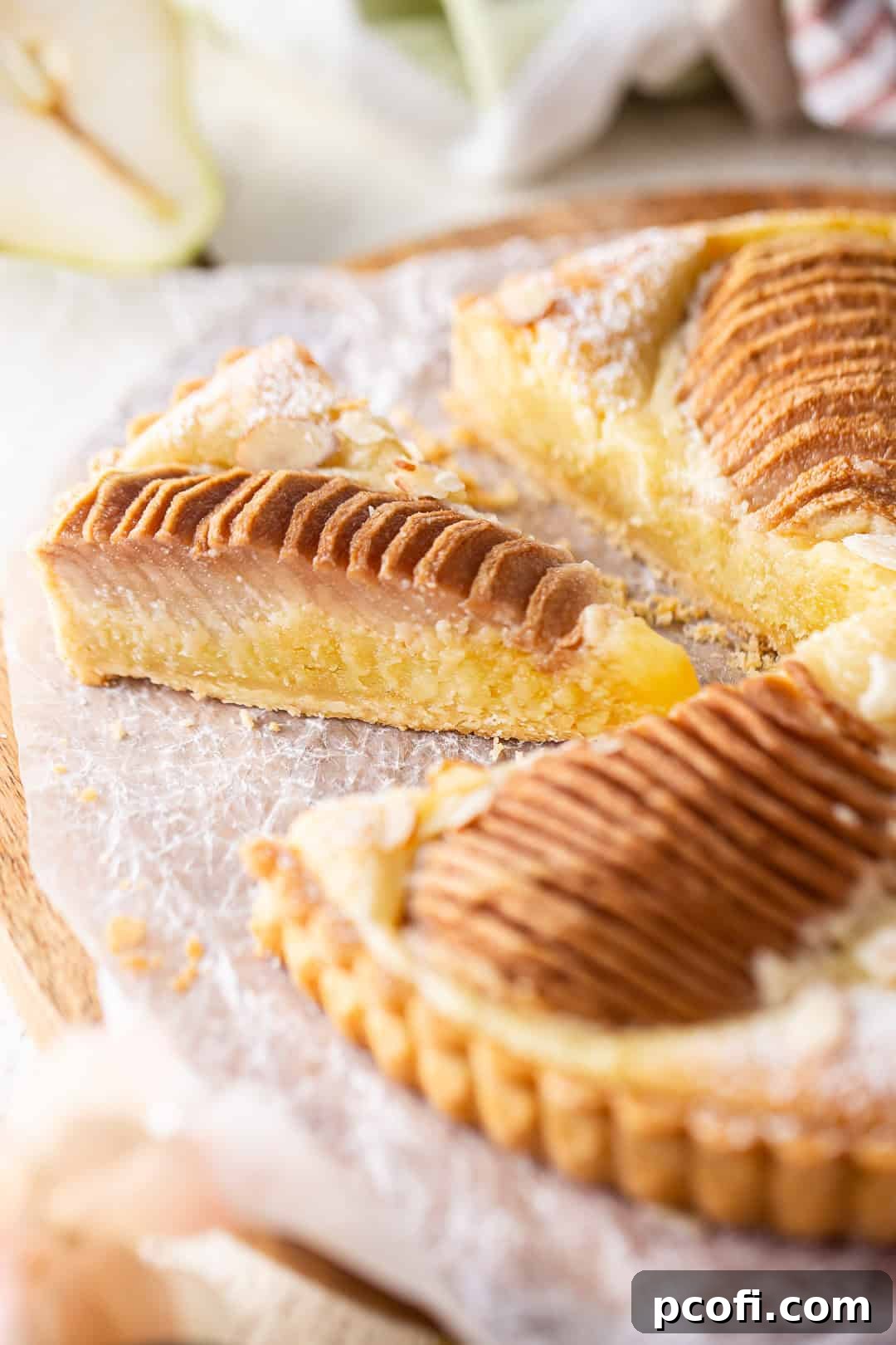 A perfectly sliced pear tart piece, revealing the layers of crust, frangipane, and tender pears.