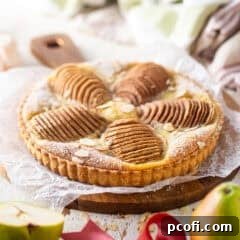 A close-up of a perfectly baked pear tart with golden crust and fanned pears, dusted with powdered sugar.