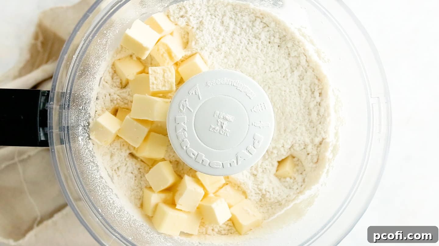 Diced cold butter being added to the dry tart crust ingredients in a food processor.