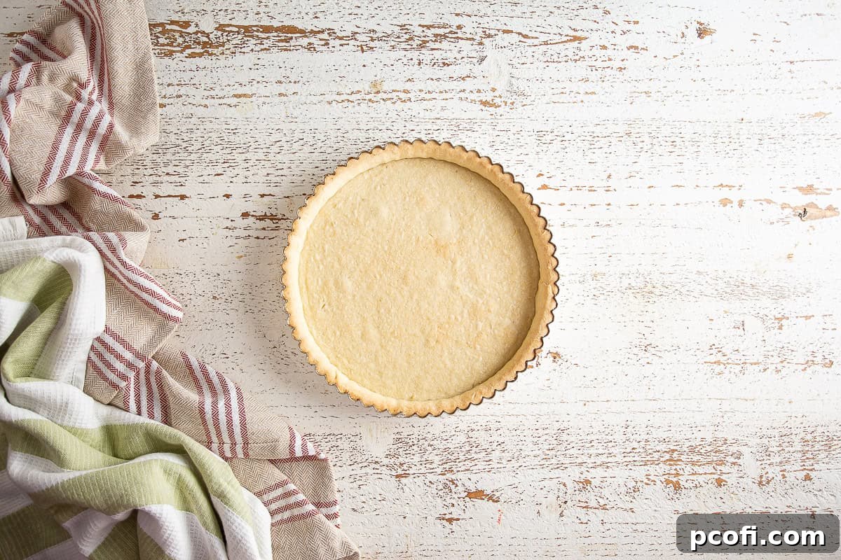 A partially baked tart crust, light golden brown around the edges, cooling on a white wooden background.