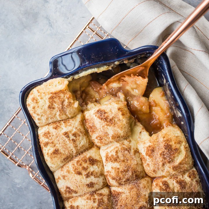 Snickerdoodle Apple Cobbler in a dark blue casserole dish, with a copper serving spoon nearby.