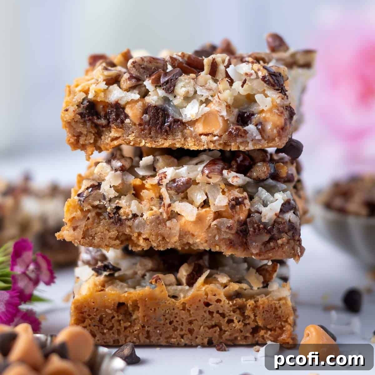 Stack of magic bars featuring a graham cracker crust, chocolate chips, butterscotch chips, pecans, and coconut, baked to golden perfection.