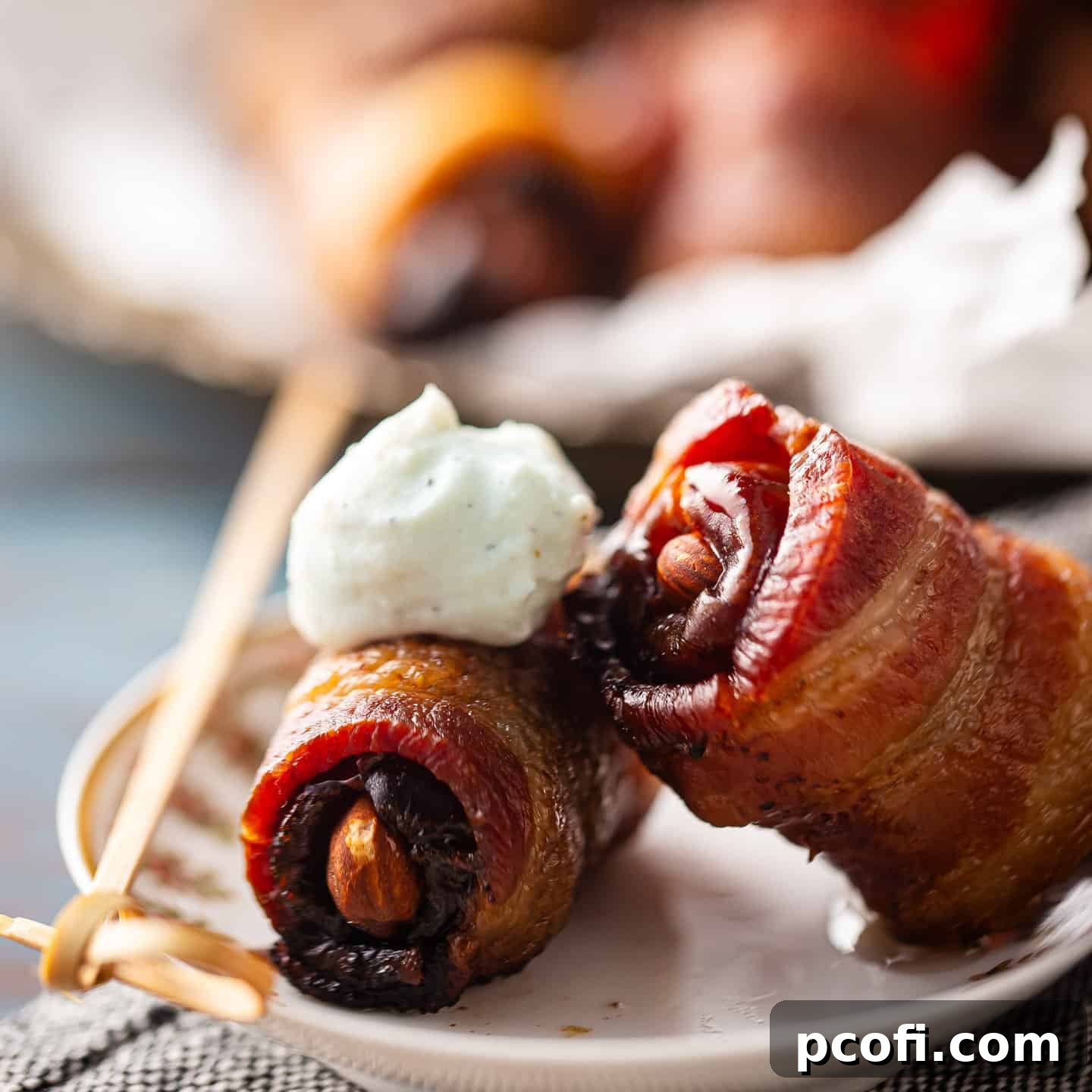 Exquisite bacon-wrapped dates, each meticulously stuffed with a crunchy almond and elegantly topped with a delicate dollop of airy whipped blue cheese, presented for an upscale appetizer experience.